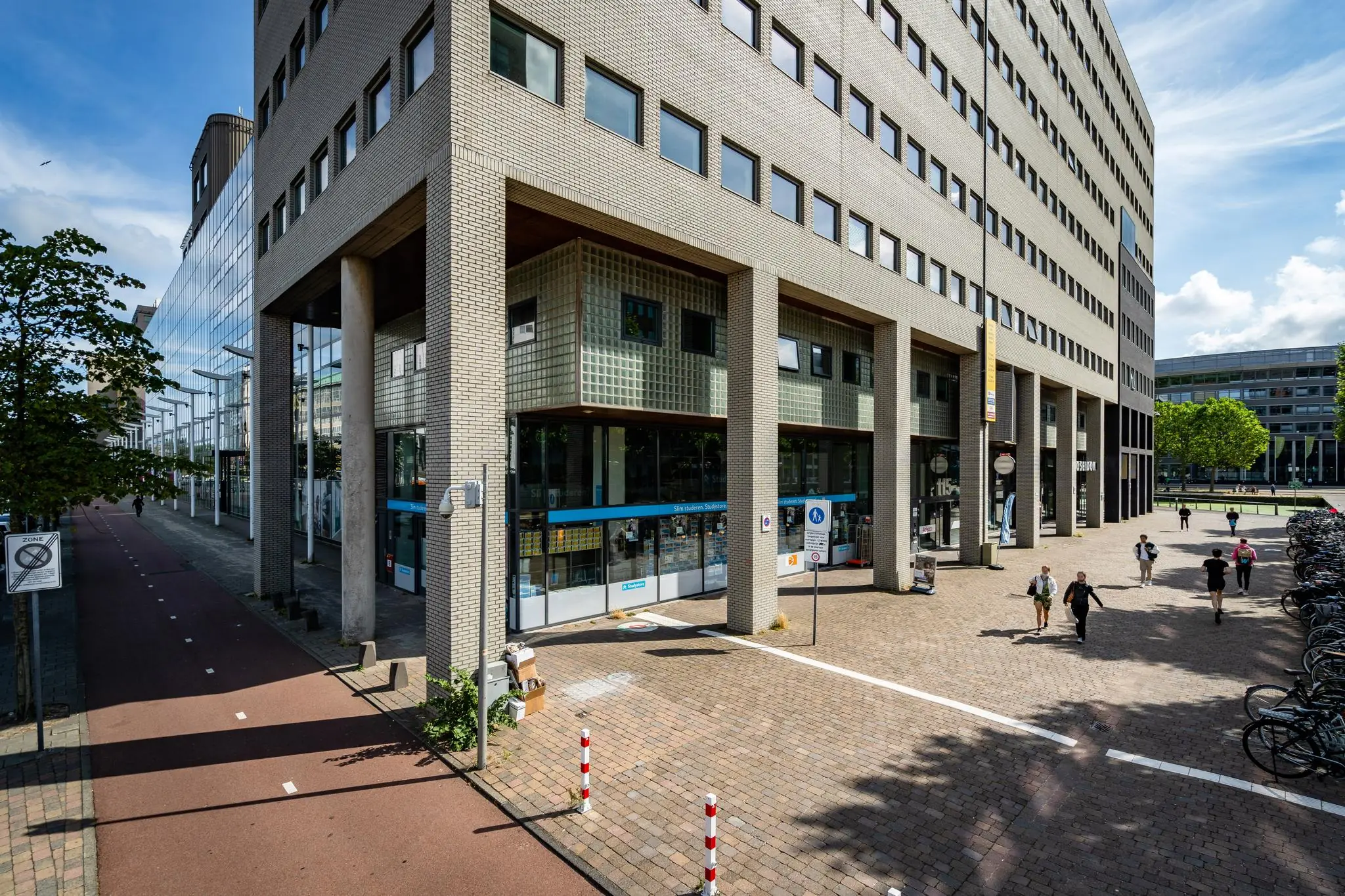 Gebouw aan het Johanna Westerdijkplein met winkels onderin en voetgangers op het plein ernaast.